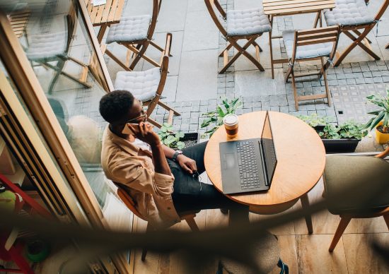 Man sitting at a table with a laptop talking on his phone 