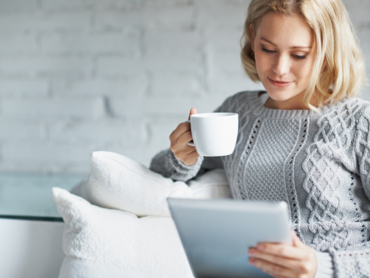 A woman sitting on the couch with a tablet and mug